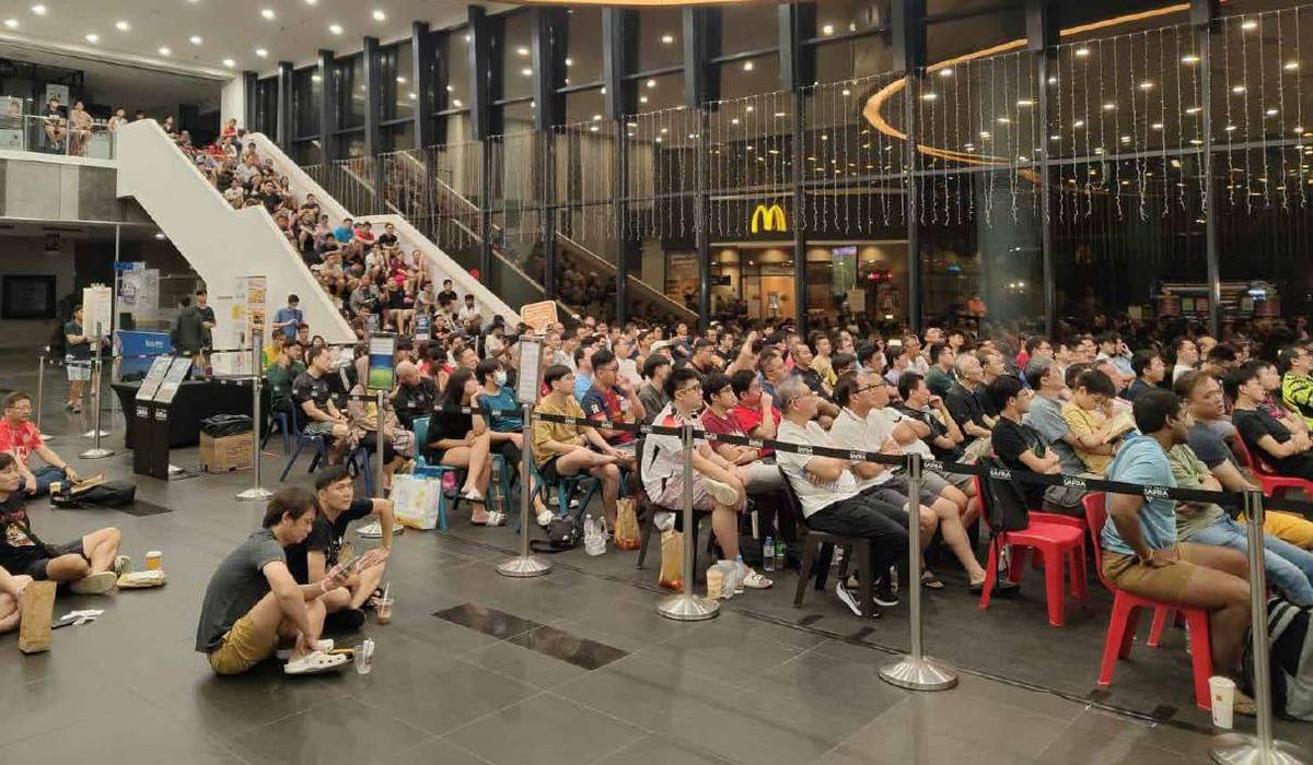 A large crowd gathered on staircase seating watching a live screen at a SAFRA community event.
